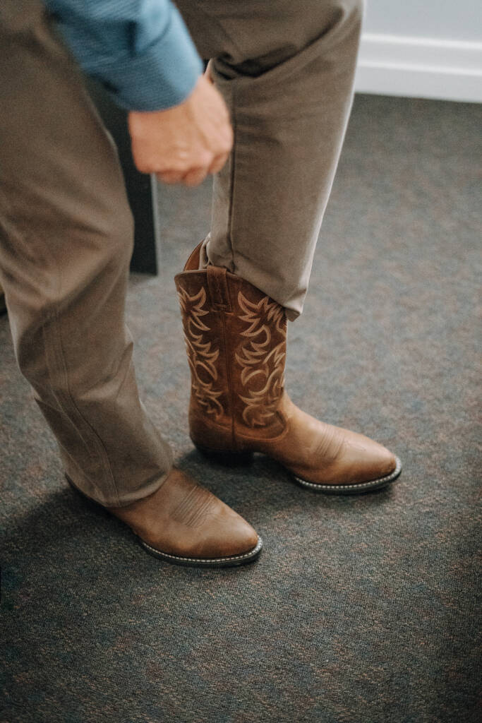 Close-up of embroidered cowboy boots beneath brown trousers during groom preparation.
