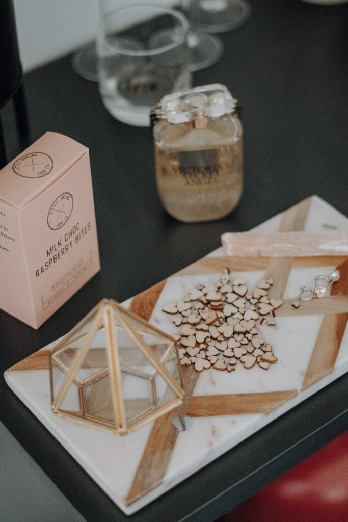 Bridal jewellery, wooden hearts and perfume are arranged beside drinks and chocolates.