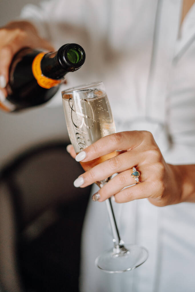 A hand holds a filled bridal flute with a bottle poised above its rim.