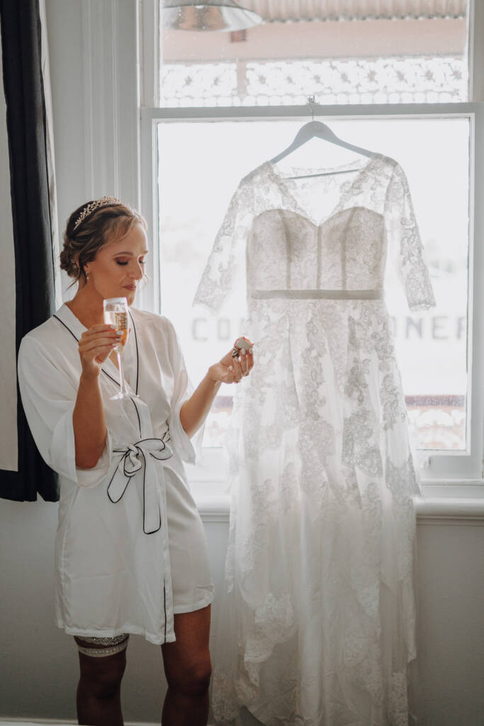 Bethany holds a flute and a small sweet beside her hanging gown at the Royal Hotel.