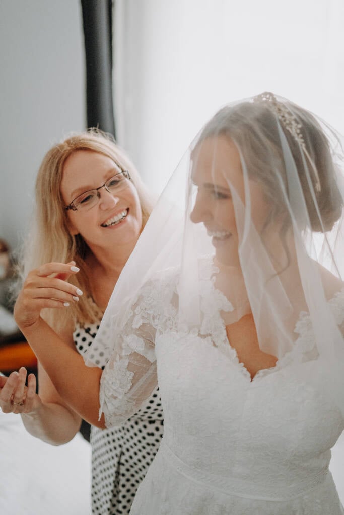 Bethany smiles beneath her veil beside a smiling guest in a patterned dress.