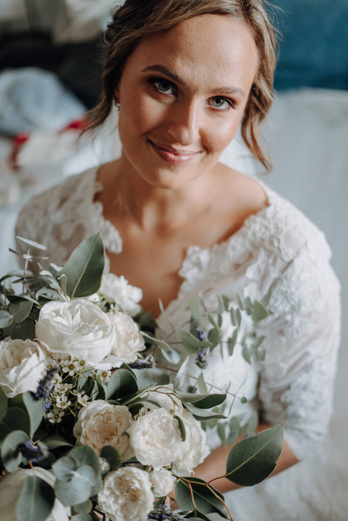 Bethany looks towards the camera above her white-flower and foliage bouquet.