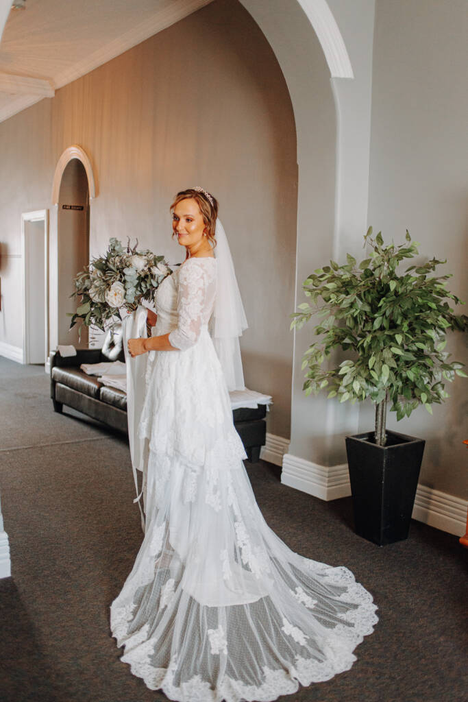 Bethany stands beneath the Royal Hotel’s hallway arch with her bouquet and lace train.