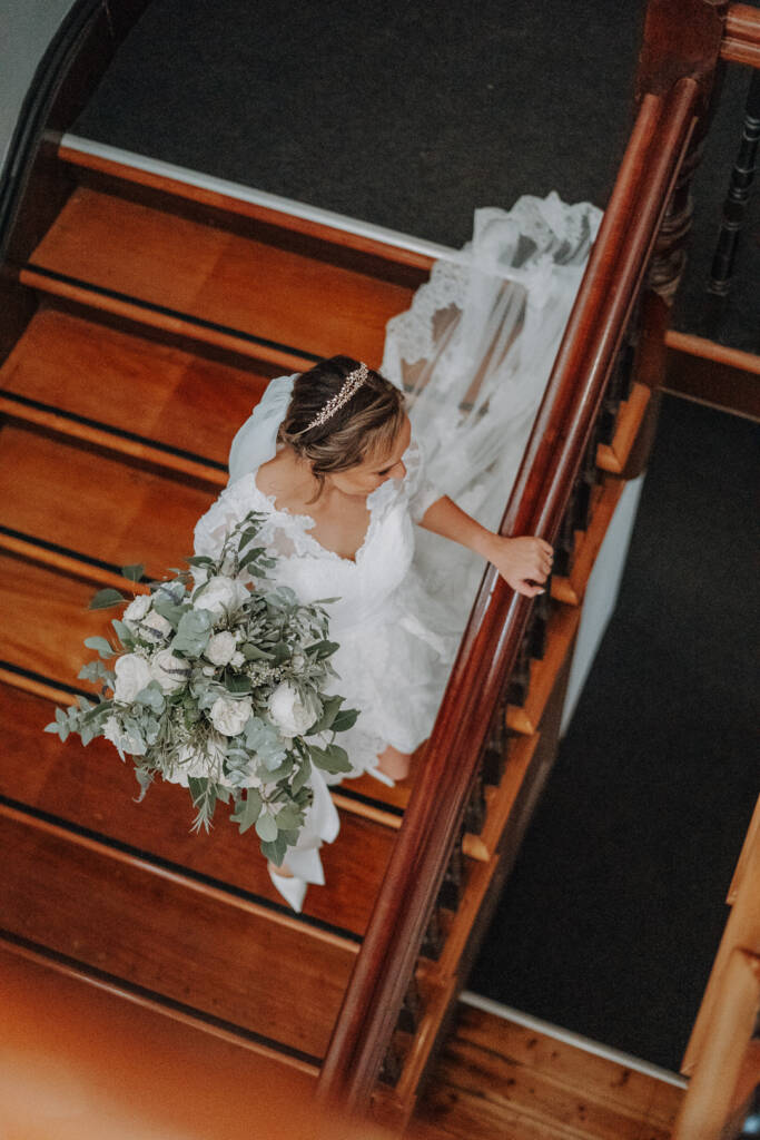 Bethany’s lace train trails behind her on the stairs at Royal Hotel Sea Lake.