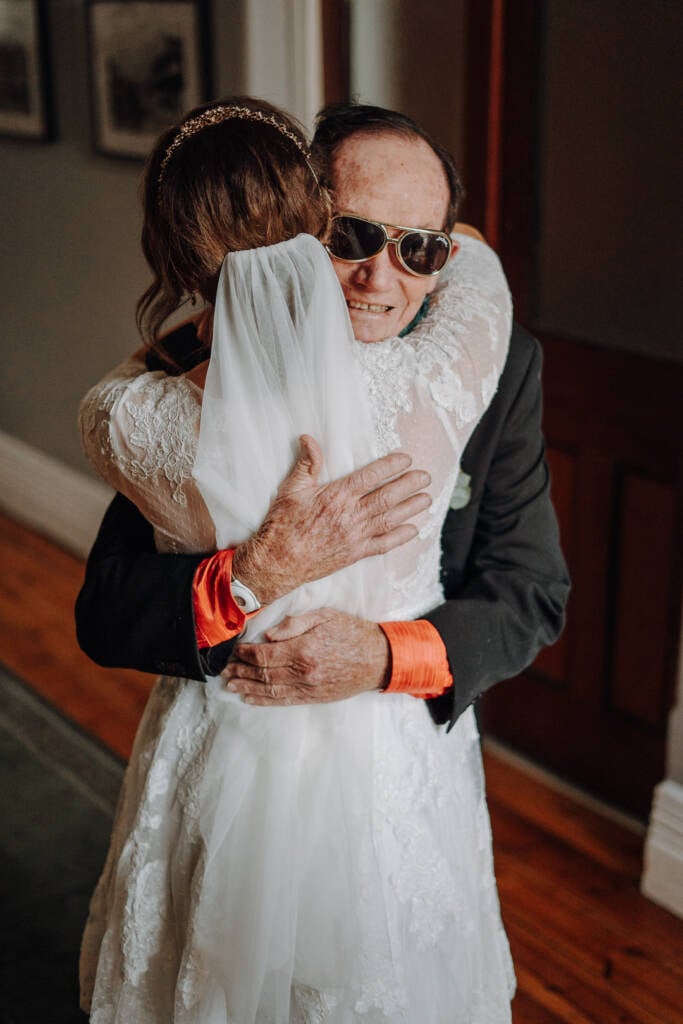 Bethany embraces a guest in a dark suit and sunglasses before the ceremony.