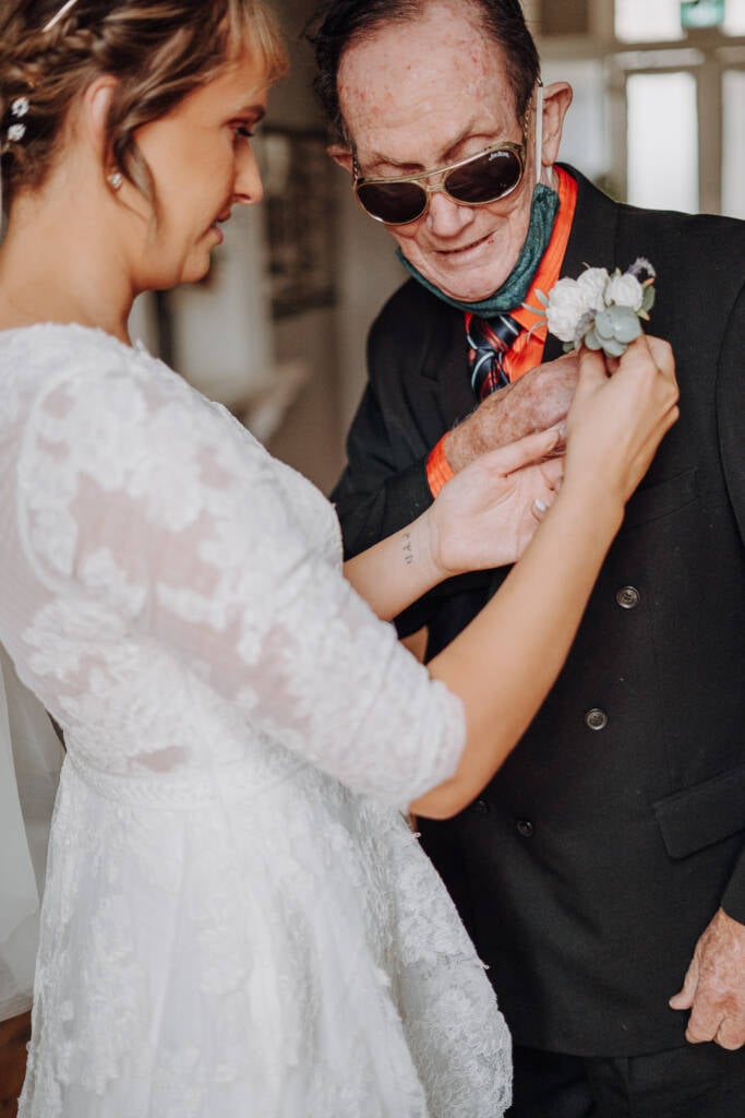 Bethany adjusts a guest’s white-flower boutonniere on his dark jacket.