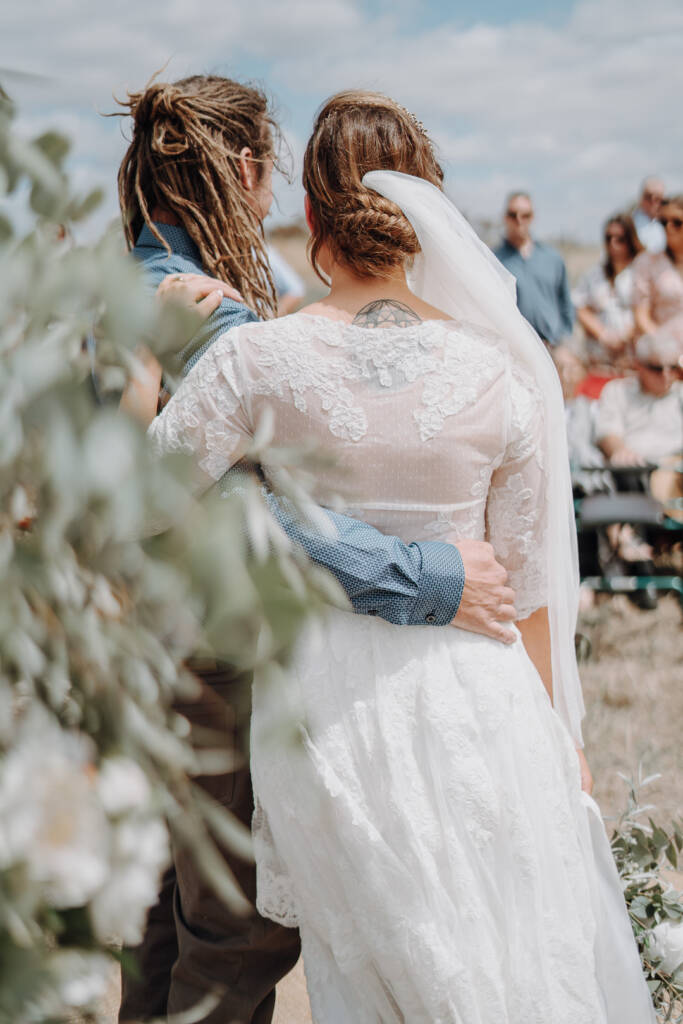 Dale stands with his arm around Bethany as her veil blows beside them.