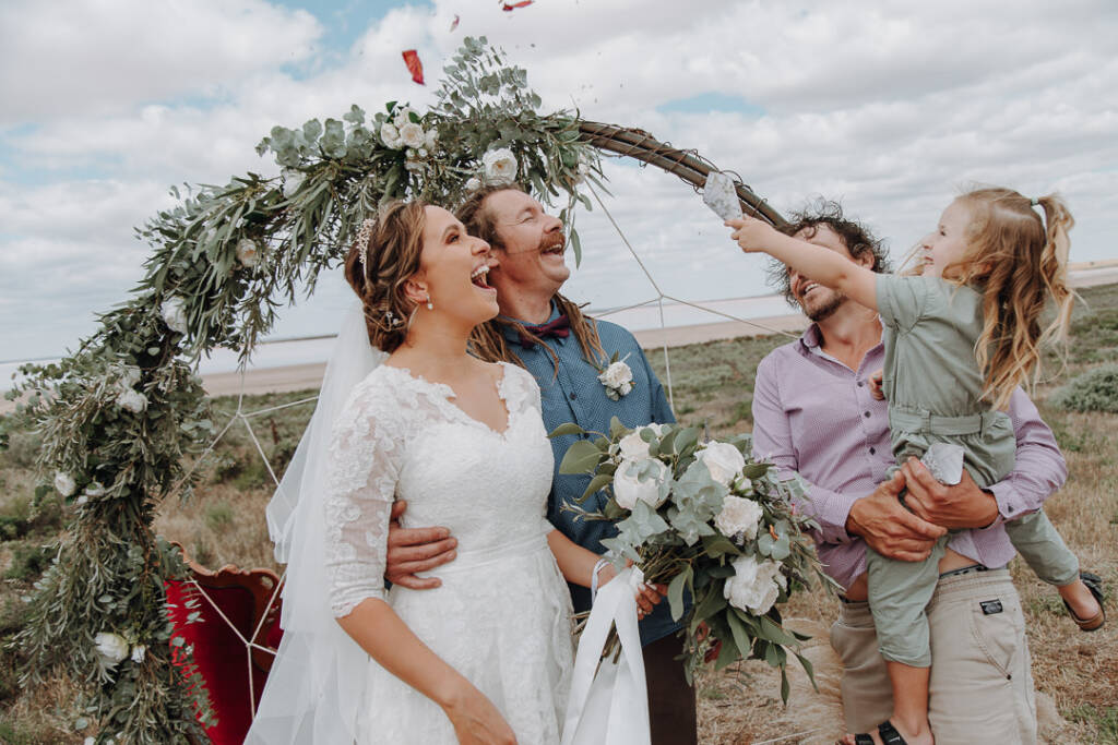 A child held by a guest scatters confetti above Bethany and Dale as they laugh.