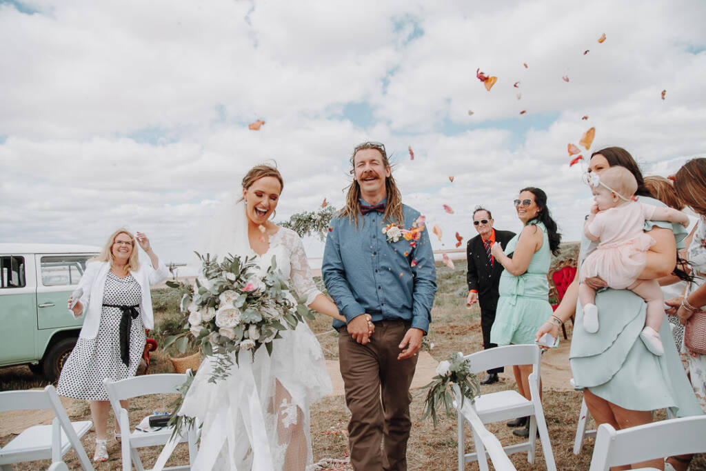 Bethany and Dale walk through falling petals after their lakeshore wedding ceremony at Lake Tyrrell.