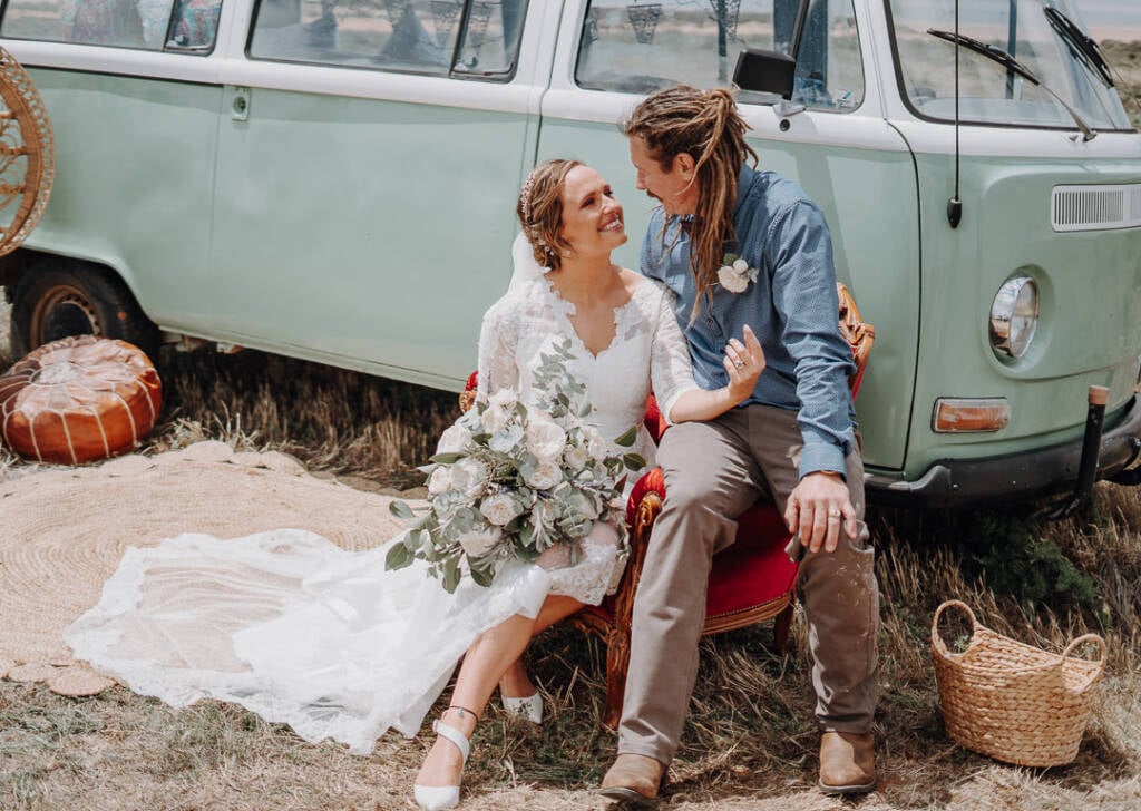Bethany and Dale share a red armchair among rugs and baskets at their Mallee country wedding beside Lake Tyrrell.