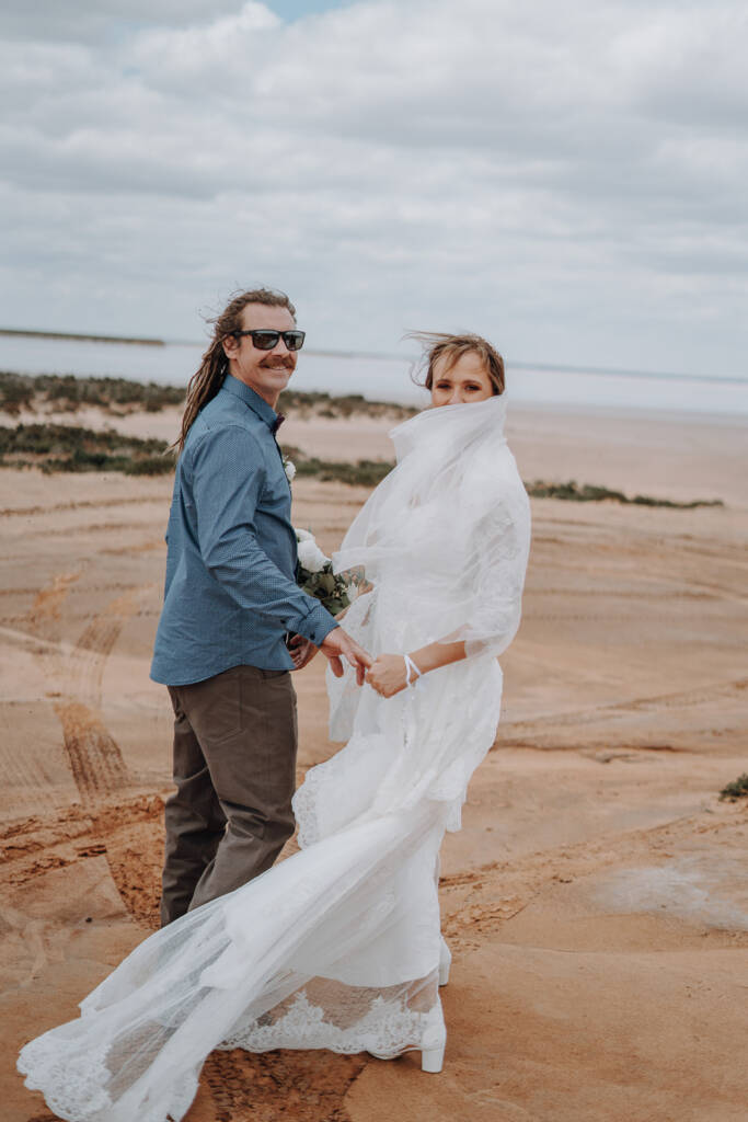 Bethany’s veil blows across her face as she holds Dale’s hand on a sandy track beside Lake Tyrrell.