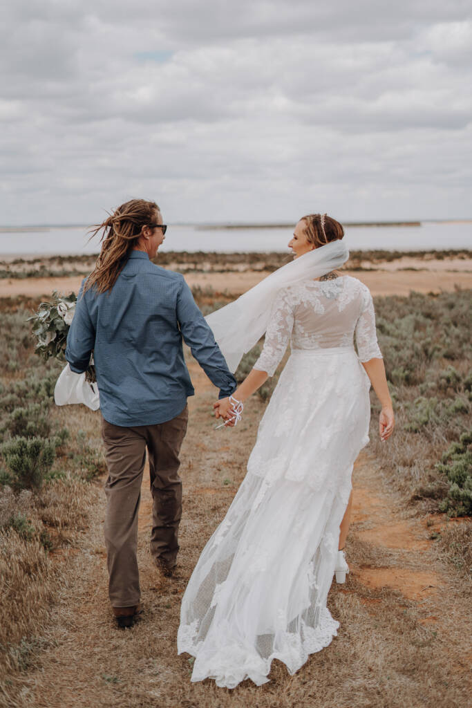 Bethany and Dale walk hand in hand through low scrub towards Lake Tyrrell’s shoreline.