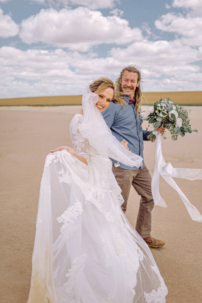 Bethany lifts her lace skirt and looks back smiling while Dale holds her bouquet.