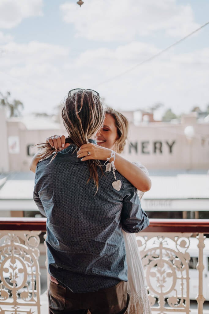 Bethany smiles with her arms around Dale beside the Royal Hotel’s balcony railing.