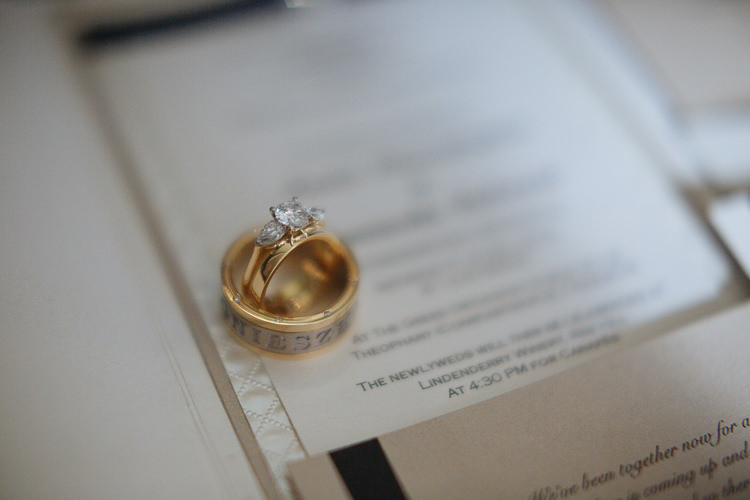 A wedding band and engagement ring rest on printed wedding stationery.