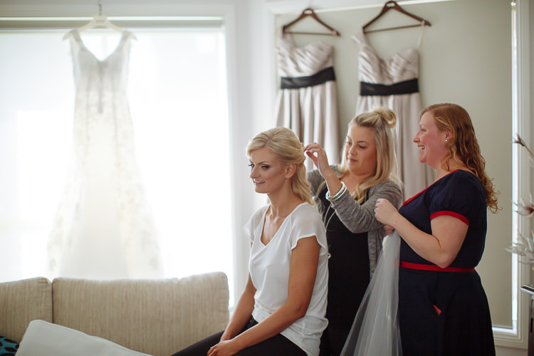 A hairstylist works on Aggie's hair while another woman holds her veil beside the hanging dresses.