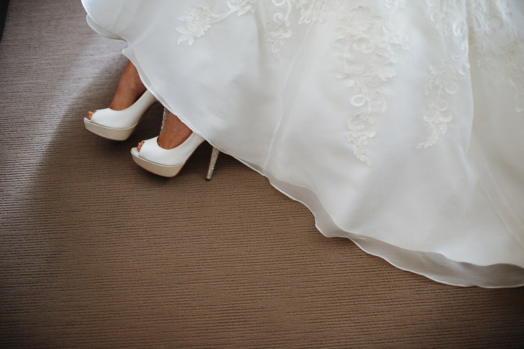 White platform peep toe heels with crystal stilettos appear beneath the lace hem of the gown.