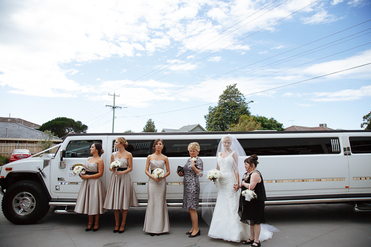 The bride stands with five women beside a white stretch limousine.
