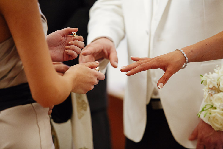 An attendant holds wedding rings beside Aggie and Alex's outstretched hands during their Greek Orthodox ceremony.