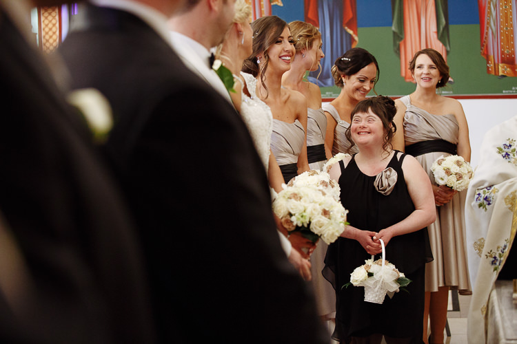 A smiling attendant holds a flower basket among bridesmaids at Holy Epiphany Greek Orthodox Church.