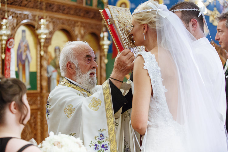 The bride kisses the ornate book held by the priest at Holy Epiphany church in Frankston.