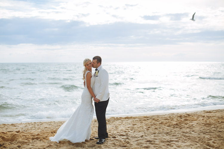 Aggie and Alex kiss beside the sea during their wedding portrait session at Frankston Beach.