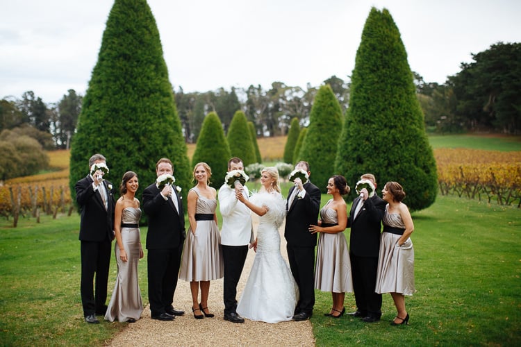 Groomsmen hold bouquets before their faces during wedding party photos at Lindenderry Red Hill.