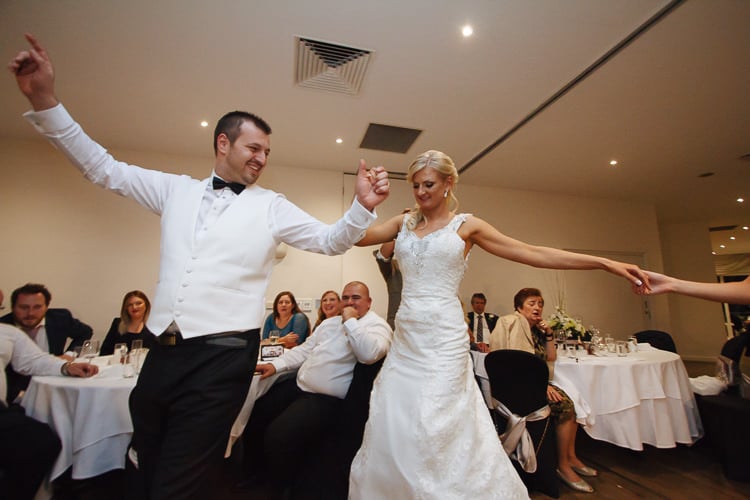 Aggie and Alex join a Greek group dance at Lindenderry Red Hill, holding hands with other guests.