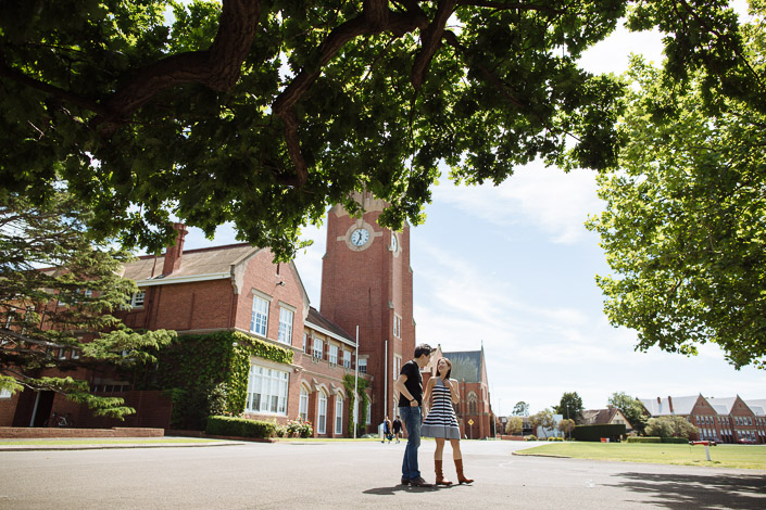 Framed by oak branches, the couple pause on the campus drive below the clock tower