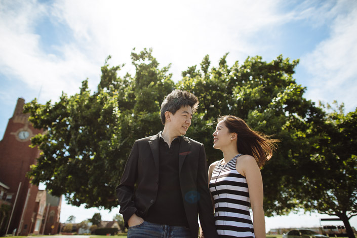 Sunlit smiles in front of a broad green canopy, the woman's striped dress catching the breeze.