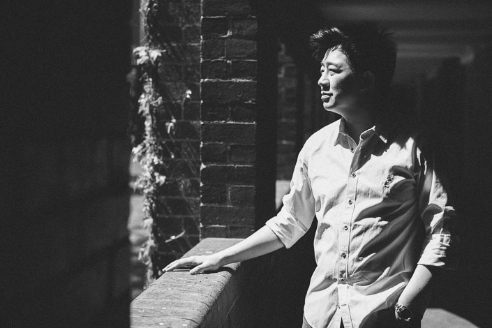 Leaning on a brick balustrade, the man turns his face into the afternoon light.