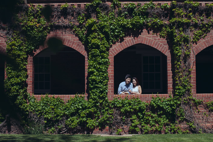 Two figures share an ivy-wrapped archway window above a sunlit lawn