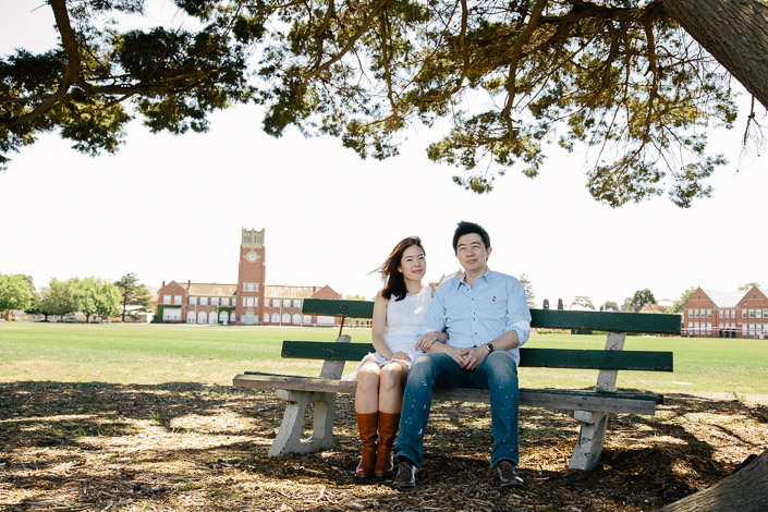 Side by side on an old park bench, the school oval and tower stretching beyond
