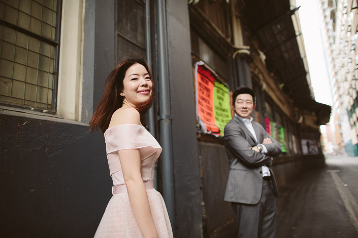 A blush off shoulder gown lights up the grey laneway as the man grins behind the woman.