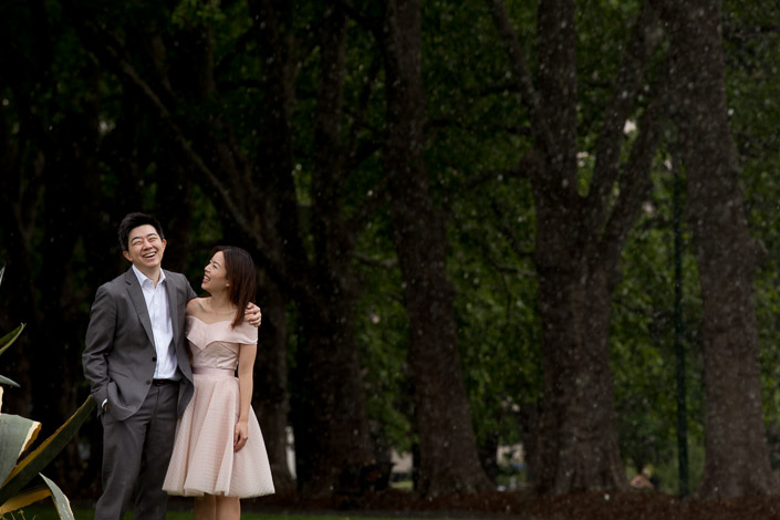 Drizzle sparkles under the dark plane trees of Carlton Gardens as the couple laugh together.