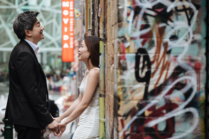 Fingers linked in graffiti splashed Hosier Lane, a neon restaurant sign glowing behind.