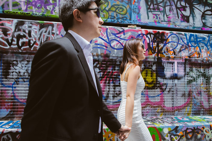 Striding past painted roller doors, the man's hand trailing back to the woman's.
