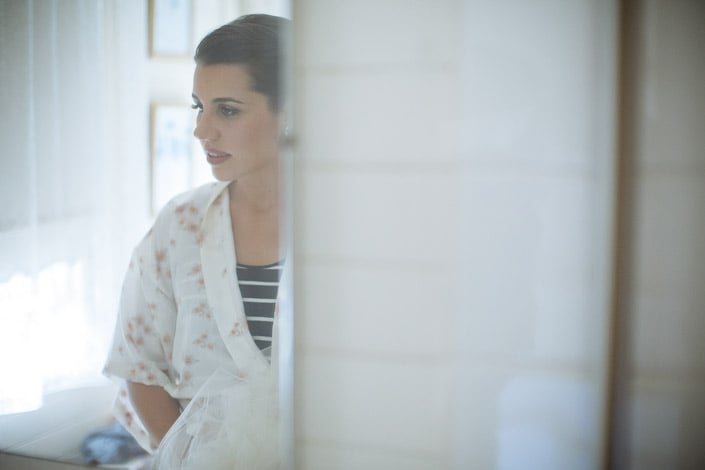 The bride sits by a window at Merrigum Cottage in Seville wearing a floral robe.