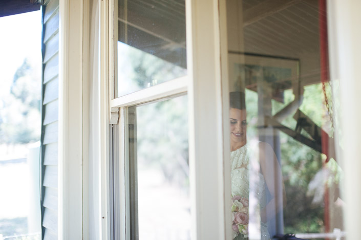 The bride looks at her bouquet through a window at Merrigum Cottage in Seville.