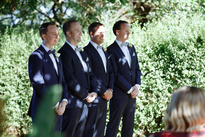 The groom and three groomsmen wait beside a hedge at Paynes Rise.