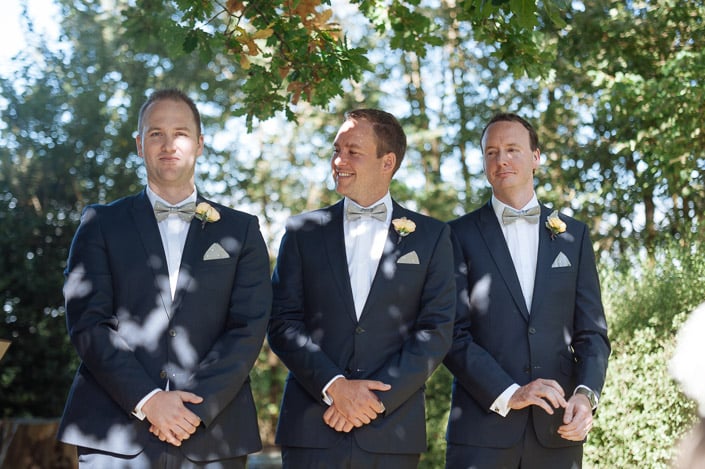 Three groomsmen in navy suits stand beneath trees at Payne’s Rise Vineyard.