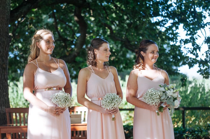 The bridesmaids look on in blush chiffon with baby's breath posies