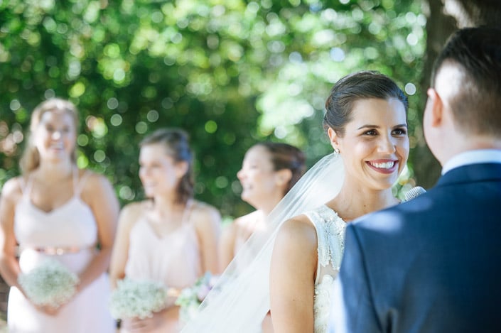 The bride smiles at the groom beneath the trees at Paynes Rise.