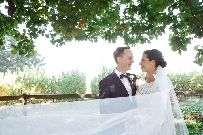 The veil sweeps across the frame as the bride and groom grin under the oak bough.