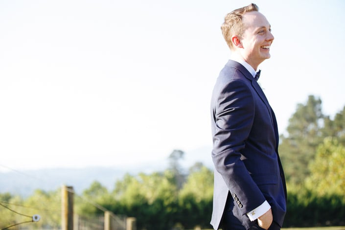 Hands in pockets, the groom laughs into the orchard breeze