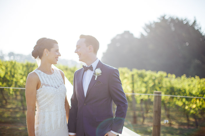 Sun haze softens the vineyard behind their shared laugh