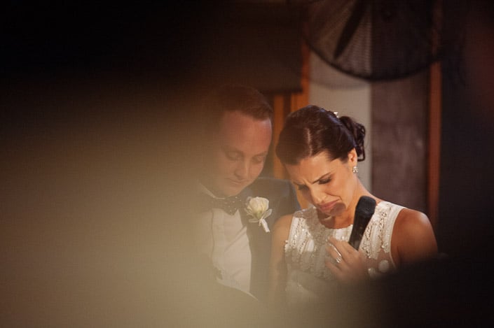 Happy tears meet the microphone below the white rose boutonniere