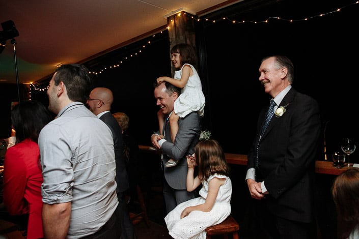 A flower girl commands the room from the shoulders of a man in a grey suit.