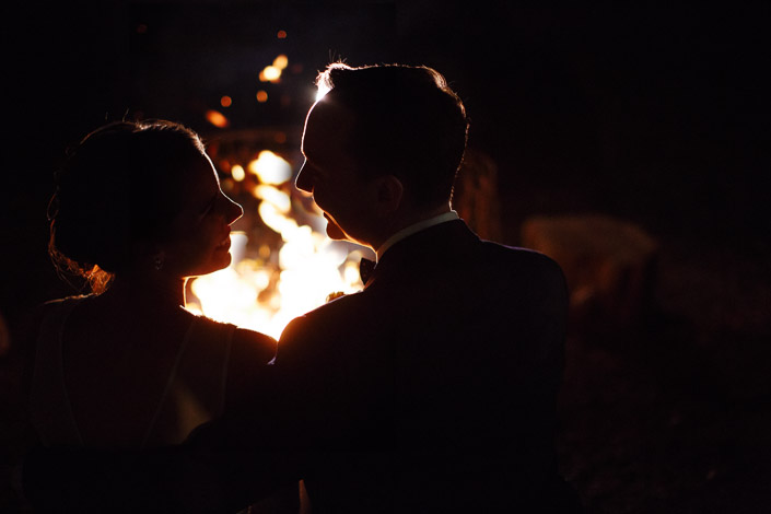 The bride and groom face each other beside a fire pit at Payne’s Rise Vineyard at night.