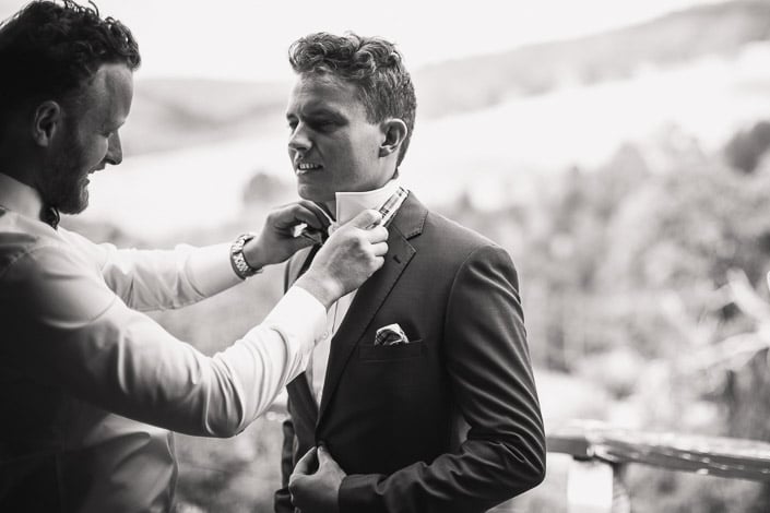 A bearded man adjusts the groom's collar before the ceremony